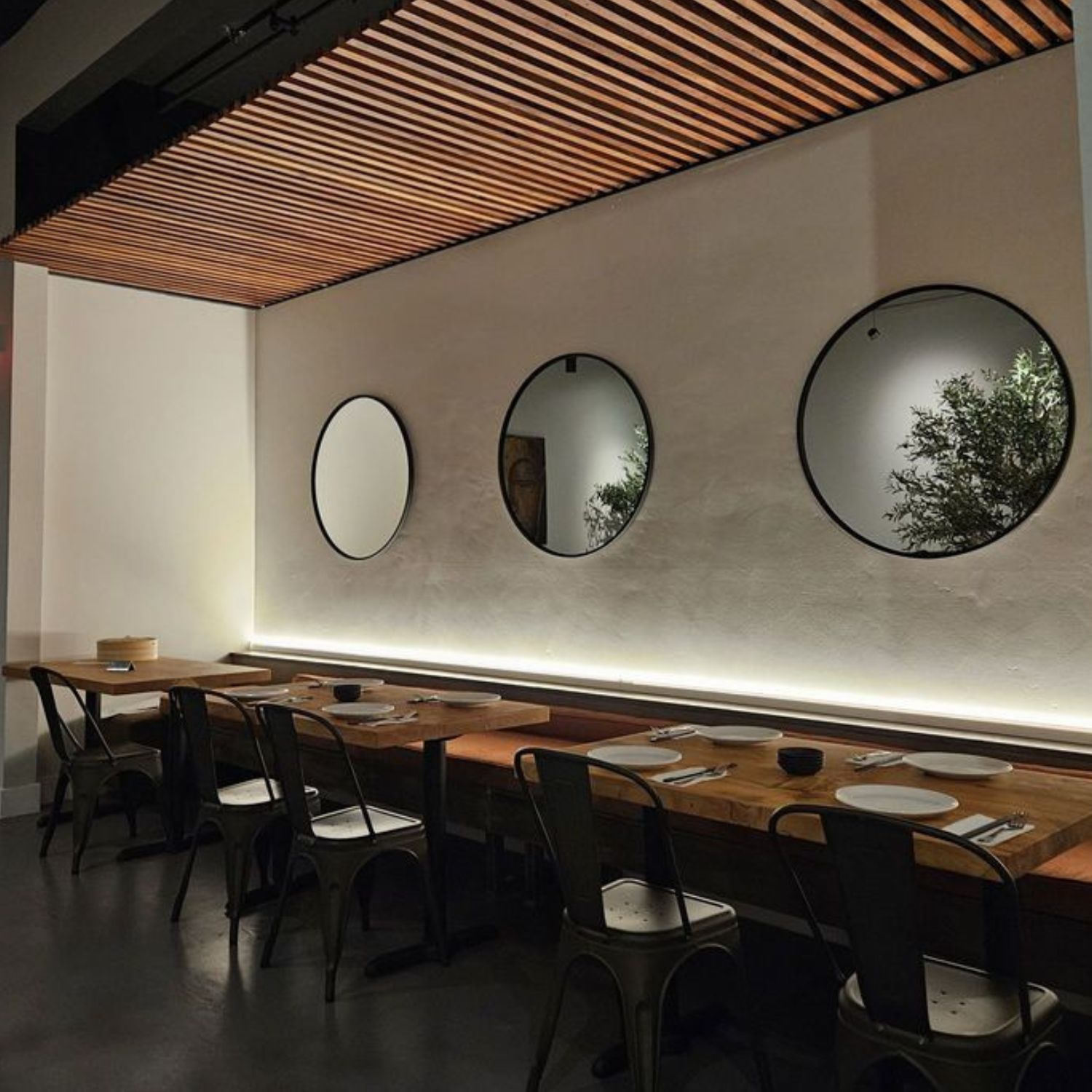 Modern dining area featuring round mirrors, warm lighting, and a slatted ceiling framed by durable high density polymer crown molding.