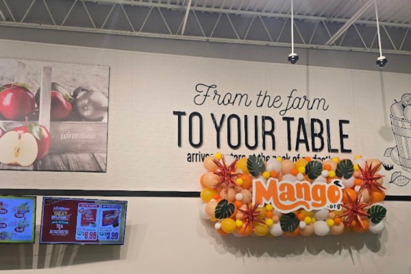 Custom painted white faux brick panels displaying farm-to-table commercial signage and a mango display in a grocery store.