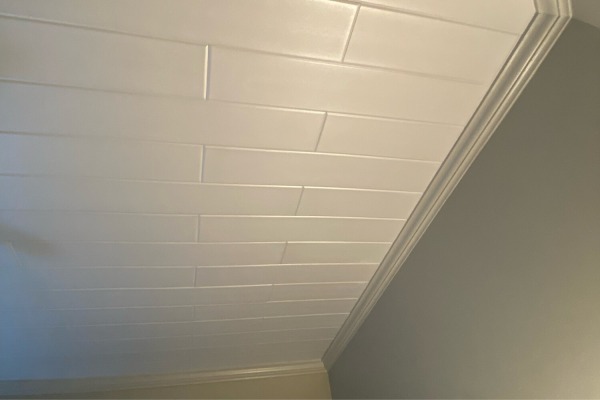 Clean edges of plain white styrofoam ceiling planks meeting elegant crown molding in a residential home makeover.