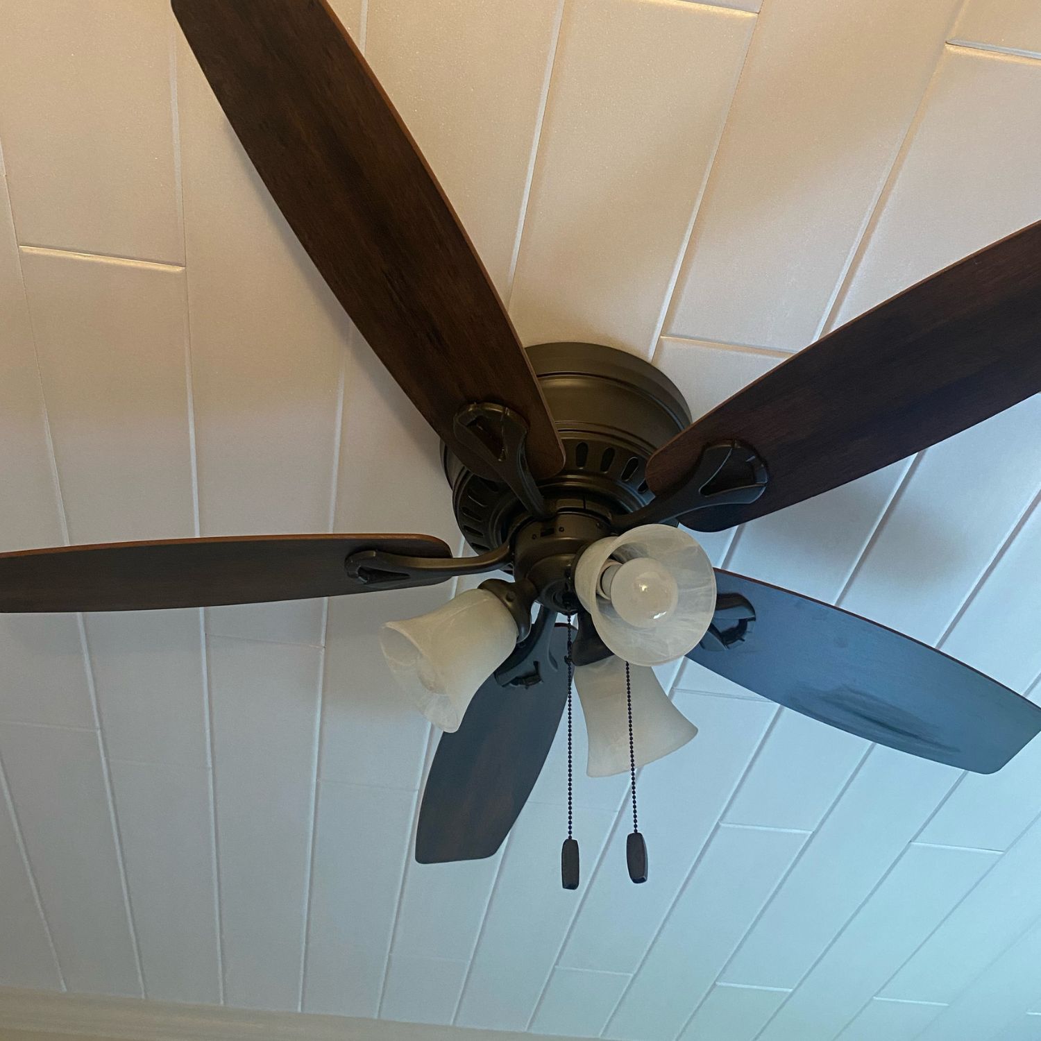 Close-up view of seamless plain white styrofoam ceiling planks installed beautifully around a dark wood ceiling fan.