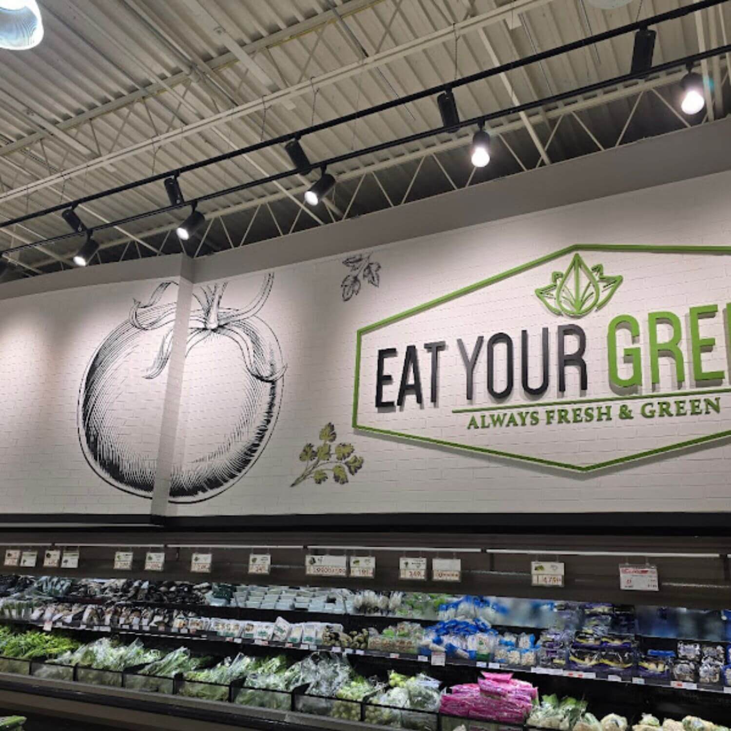 White faux brick wall panels serving as a textured backdrop for "Eat Your Greens" signage in a supermarket produce section.
