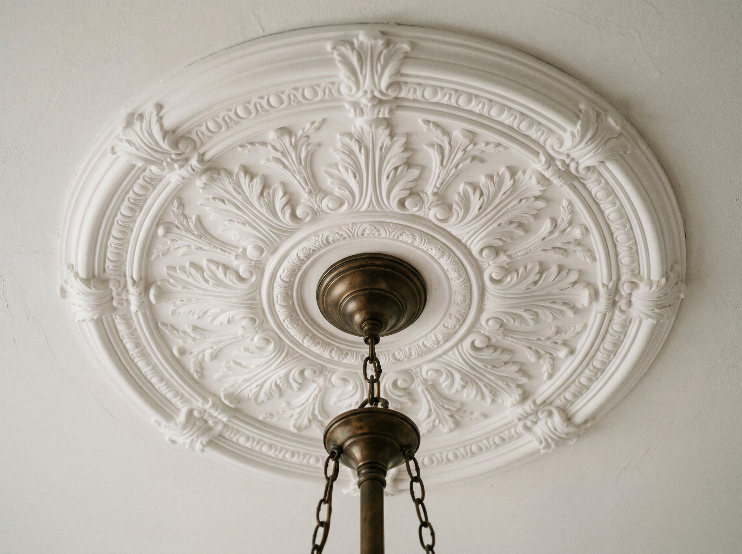 Large white ornate ceiling medallion installed around a bronze pendant light