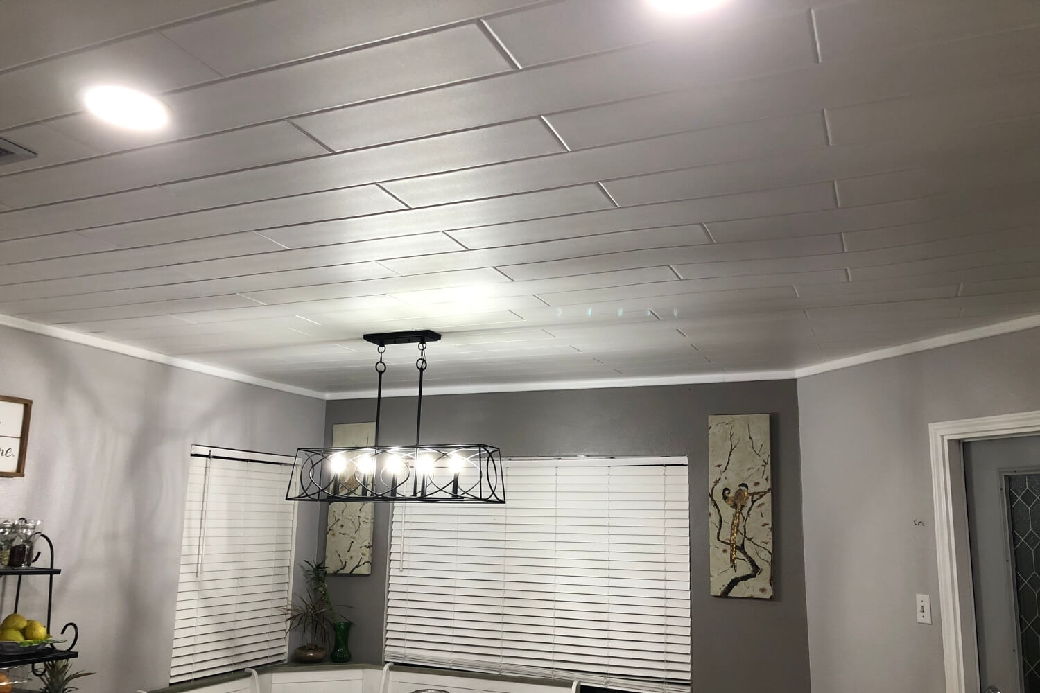 Modern dining room featuring plain white styrofoam ceiling planks, grey walls, and a black chandelier.