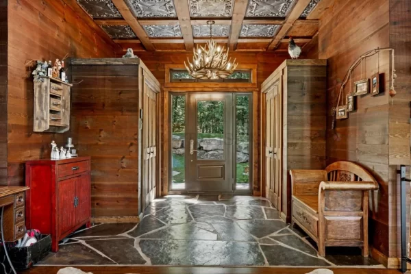 Full view of a beautiful cabin foyer showcasing rich wood-paneled walls, stone flooring, and a decorative aged silver tin ceiling overhead.