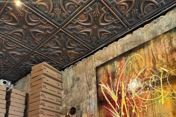 The ordering counter at a Downtown Toronto pizzeria featuring artistic walls, pizza boxes, and elegant smoked copper tin ceiling tiles.
