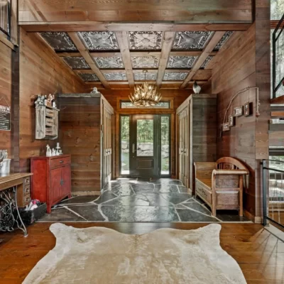 A grand rustic lodge entrance in Sherbrooke, QC, featuring an antler chandelier and stunning TD22 Aged Silver tin ceiling tiles installed between wooden beams.