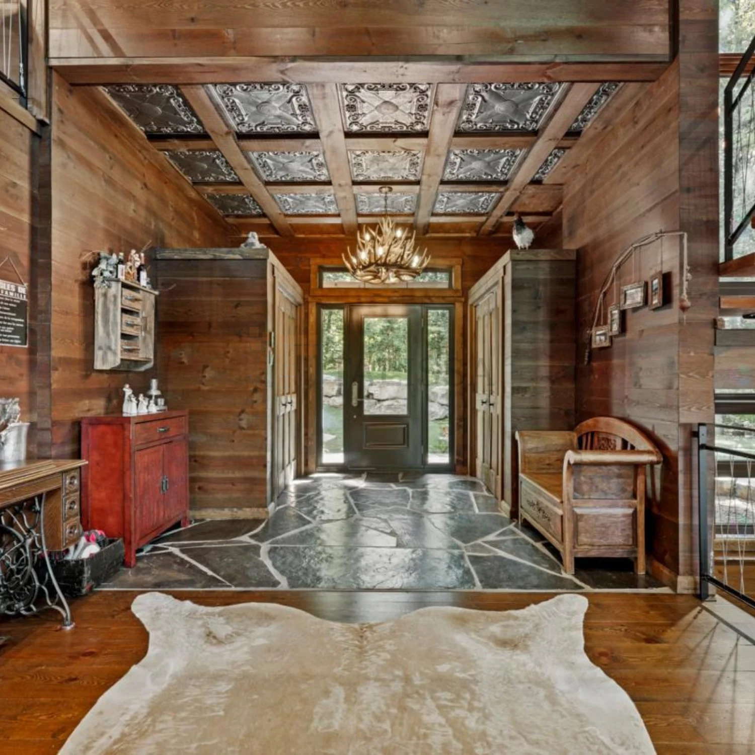 A grand rustic lodge entrance in Sherbrooke, QC, featuring an antler chandelier and stunning TD22 Aged Silver tin ceiling tiles installed between wooden beams.