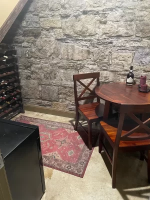 Castle Stones stone-look wall mural behind a wine rack, bistro table and red rug in a Toronto, ON home bar under the stairs