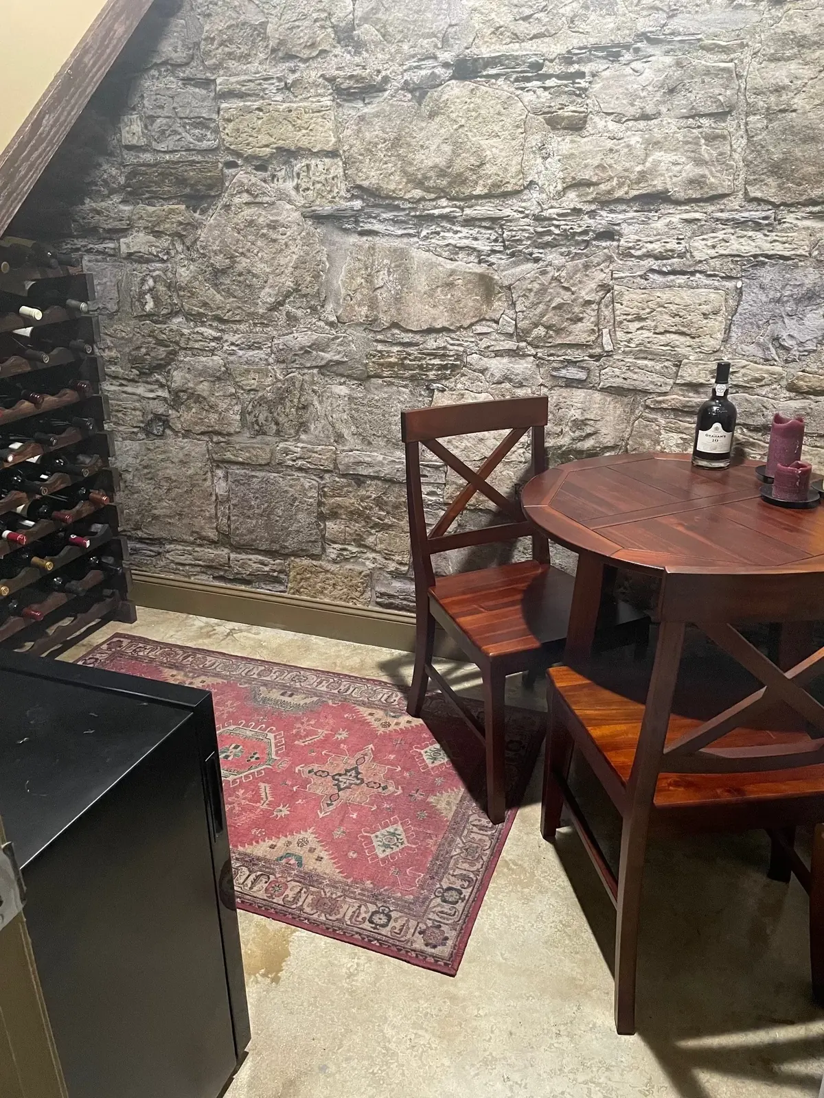 Castle Stones stone-look wall mural behind a wine rack, bistro table and red rug in a Toronto, ON home bar under the stairs