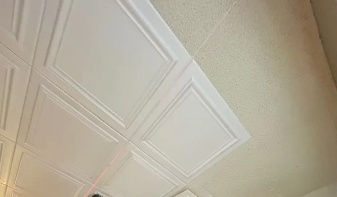 RM24 ceiling tiles glued over a textured popcorn ceiling, with a laser line guiding the next row